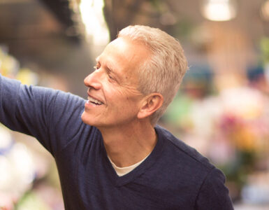 A middle-aged man reaching for fresh peppers in the grocery store.