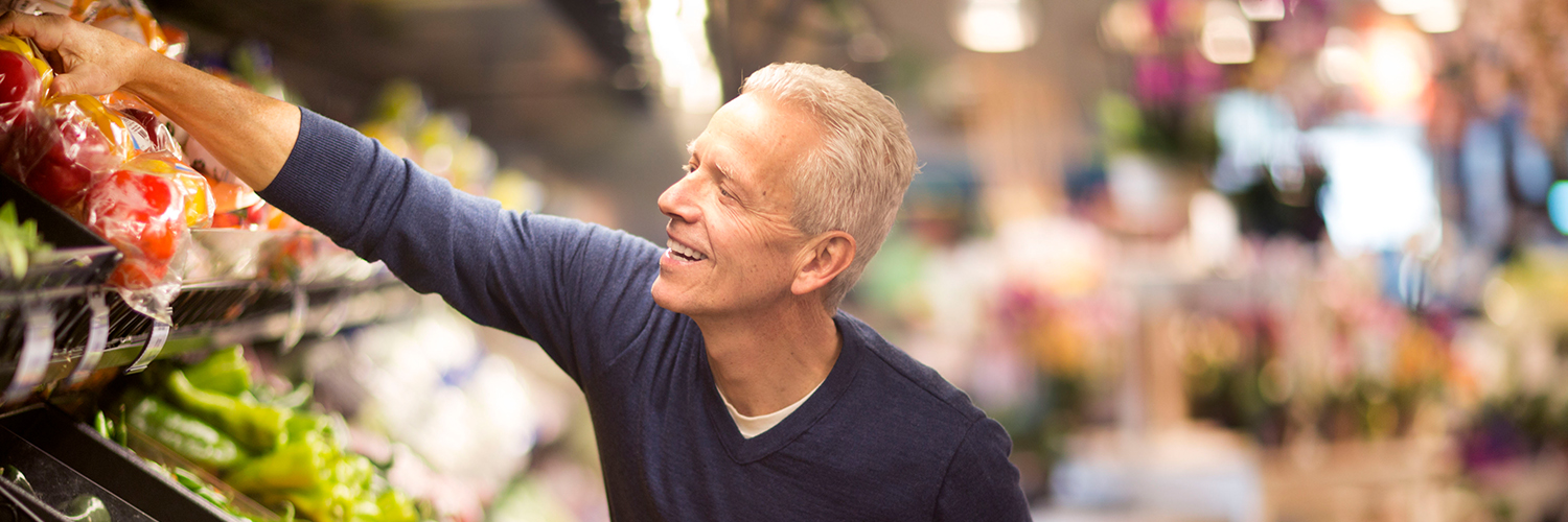 A middle-aged man reaching for fresh peppers in the grocery store.