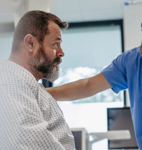 A middle-aged man awaiting surgery in the hospital, with his doctor's hand on his shoulder.