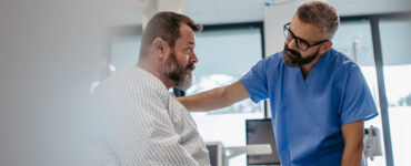 A middle-aged man awaiting surgery in the hospital, with his doctor's hand on his shoulder.