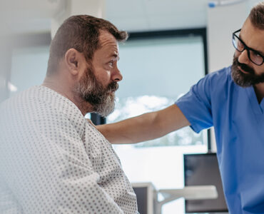 A middle-aged man awaiting surgery in the hospital, with his doctor's hand on his shoulder.