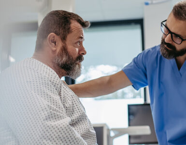 A middle-aged man awaiting surgery in the hospital, with his doctor's hand on his shoulder.