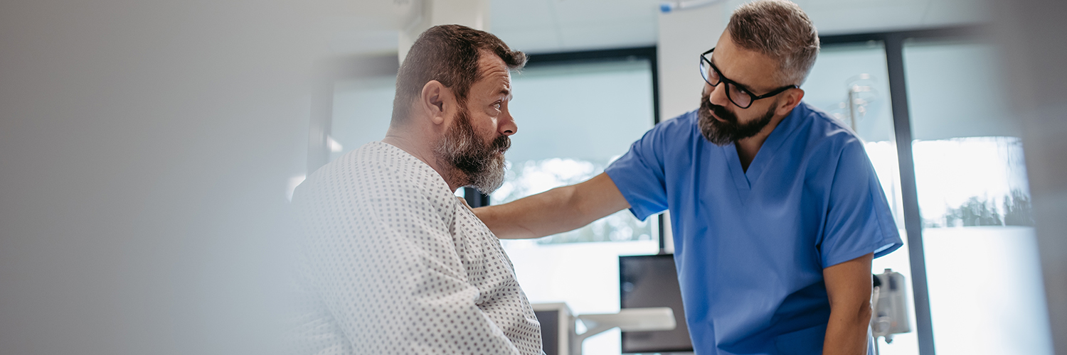 A middle-aged man awaiting surgery in the hospital, with his doctor's hand on his shoulder.