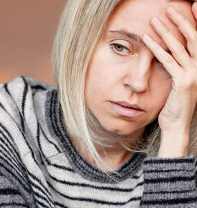 A grieving woman sitting on her couch alone, with her hand to her forehead.