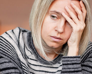 A grieving woman sitting on her couch alone, with her hand to her forehead.