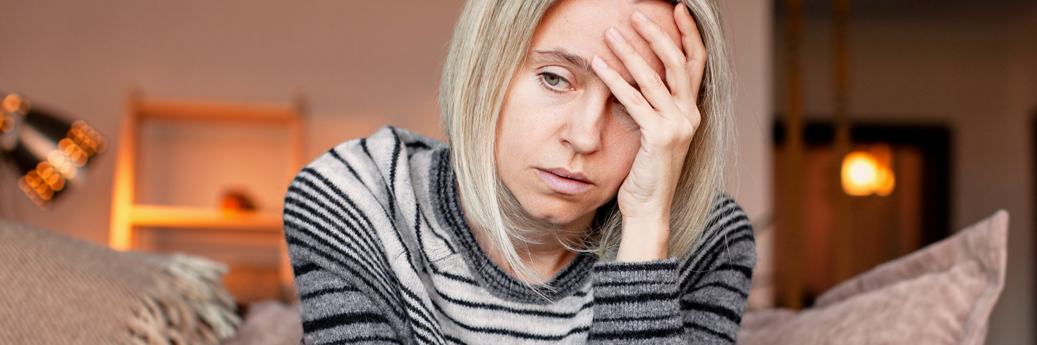 A grieving woman sitting on her couch alone, with her hand to her forehead.