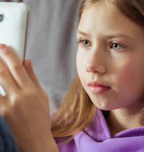A tween girl sitting on her couch, looking directly at her smartphone.