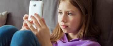 A tween girl sitting on her couch, looking directly at her smartphone.