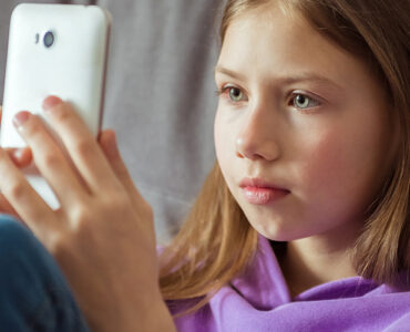 A tween girl sitting on her couch, looking directly at her smartphone.