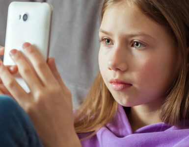 A tween girl sitting on her couch, looking directly at her smartphone.
