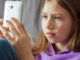 A tween girl sitting on her couch, looking directly at her smartphone.