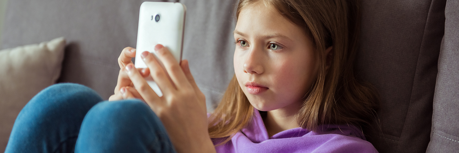 A tween girl sitting on her couch, looking directly at her smartphone.