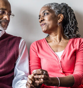 An older black woman holding her husband's and looking into his eyes.