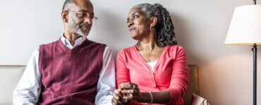 An older black woman holding her husband's and looking into his eyes.