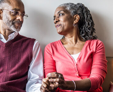 An older black woman holding her husband's and looking into his eyes.