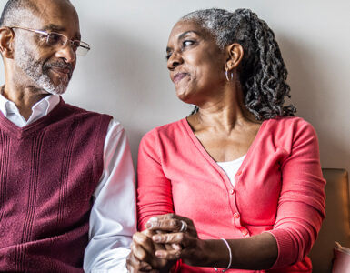 An older black woman holding her husband's and looking into his eyes.