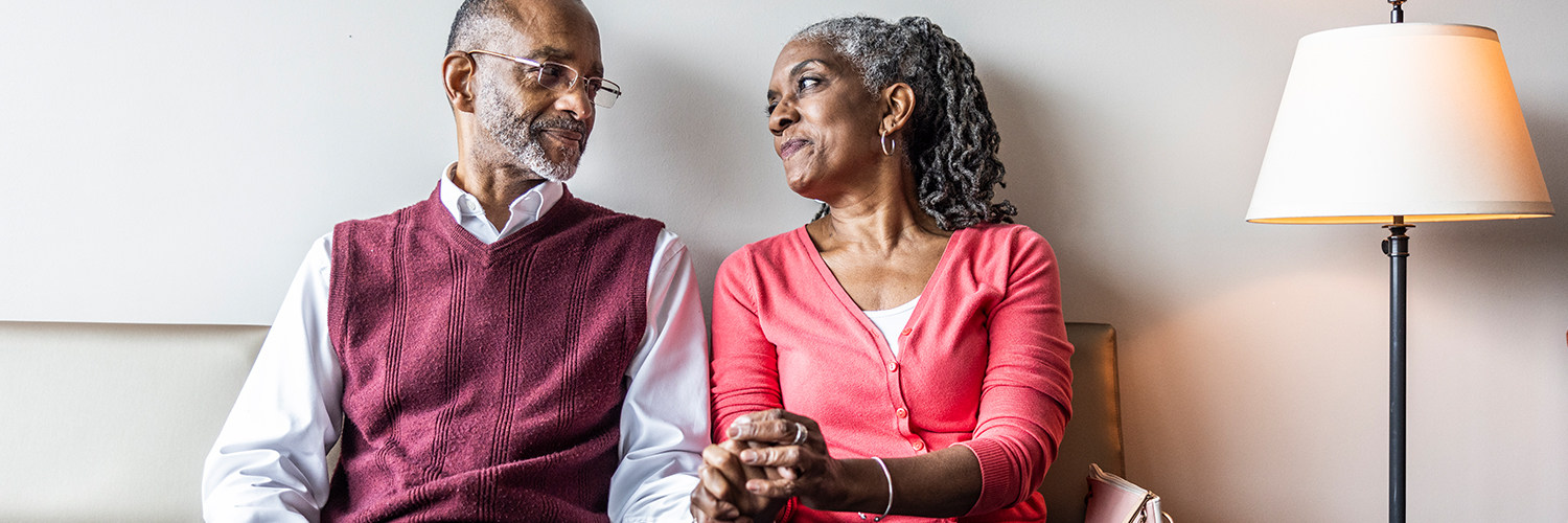 An older black woman holding her husband's and looking into his eyes.