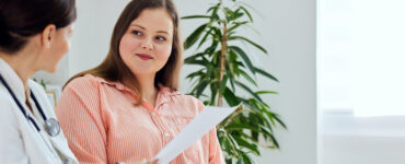 A woman in her 40s sitting next to her doctor with a slight smile as they review paperwork.
