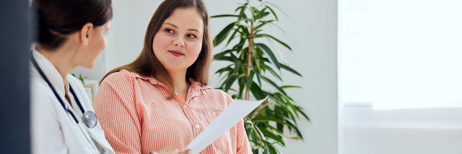 A woman in her 40s sitting next to her doctor with a slight smile as they review paperwork.
