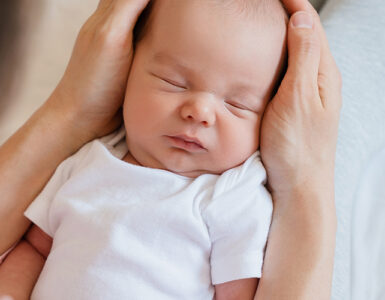 A newborn baby sleeping in his mother's arms.