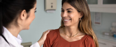 A middle-aged woman standing with her primary care doctor, smiling.
