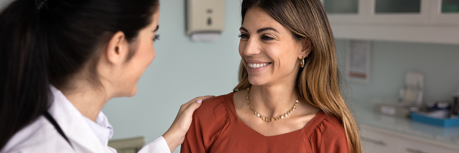 A middle-aged woman standing with her primary care doctor, smiling.
