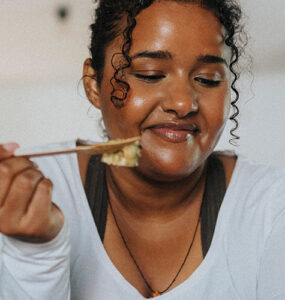A young black woman leaning over her kitchen island while eating a salad.