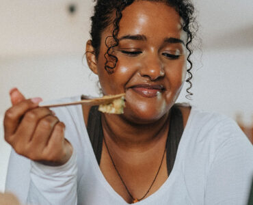 A young black woman leaning over her kitchen island while eating a salad.