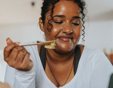 A young black woman leaning over her kitchen island while eating a salad.