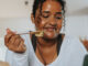 A young black woman leaning over her kitchen island while eating a salad.