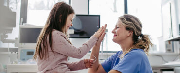 A young girl sitting with a nurse, high-fiving one another while smiling.