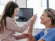 A young girl sitting with a nurse, high-fiving one another while smiling.