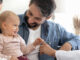A baby smiling and sitting with her parents, alongside their pediatrician who is touching the baby's hand.