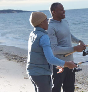 A father and his young son standing on the shoreline during sunset, with a fishing pole in the Long Island Sound.