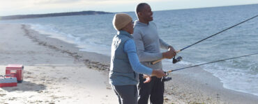 A father and his young son standing on the shoreline during sunset, with a fishing pole in the Long Island Sound.