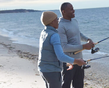 A father and his young son standing on the shoreline during sunset, with a fishing pole in the Long Island Sound.