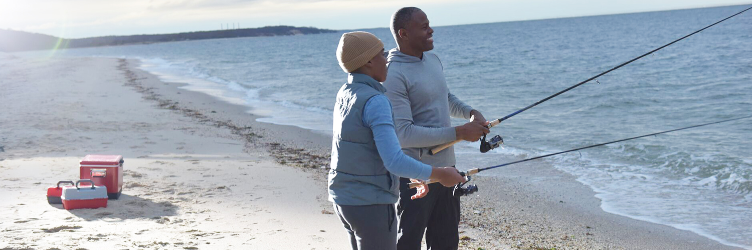 A father and his young son standing on the shoreline during sunset, with a fishing pole in the Long Island Sound.