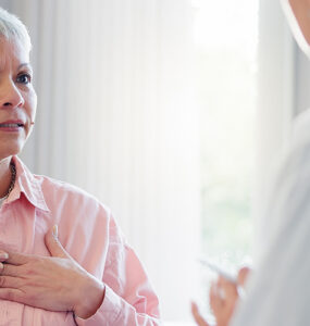 An older woman in her doctor's office, holding her heart while in a conversation.