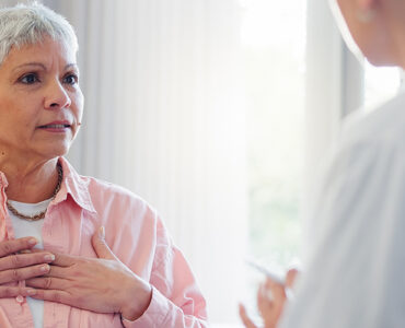 An older woman in her doctor's office, holding her heart while in a conversation.