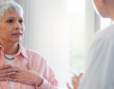 An older woman in her doctor's office, holding her heart while in a conversation.