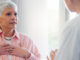 An older woman in her doctor's office, holding her heart while in a conversation.