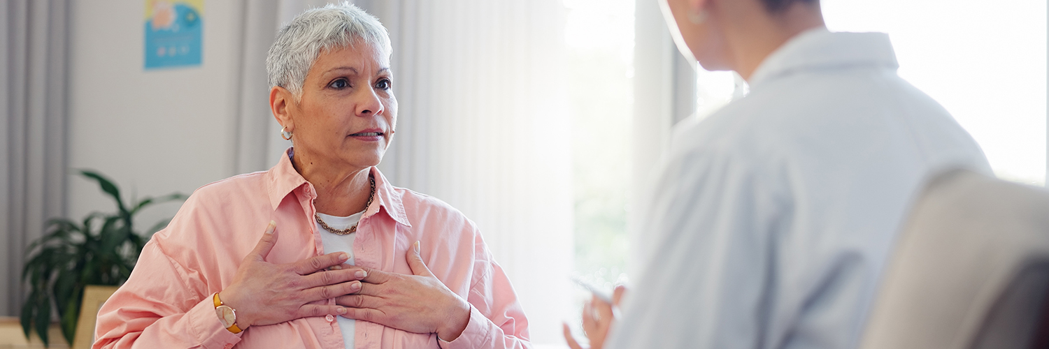 An older woman in her doctor's office, holding her heart while in a conversation.