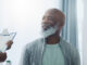 An older black man sitting in a medical office, smiling at the nurse who is holding a clipboard.