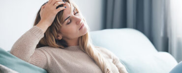 A woman sitting on couch with hand on head.