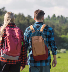 A young man and woman walking outdoors past a sign with a tick icon on it.