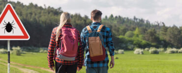 A young man and woman walking outdoors past a sign with a tick icon on it.