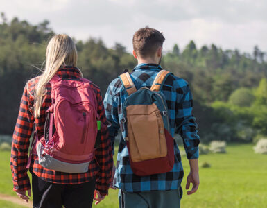 A young man and woman walking outdoors past a sign with a tick icon on it.