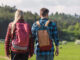 A young man and woman walking outdoors past a sign with a tick icon on it.