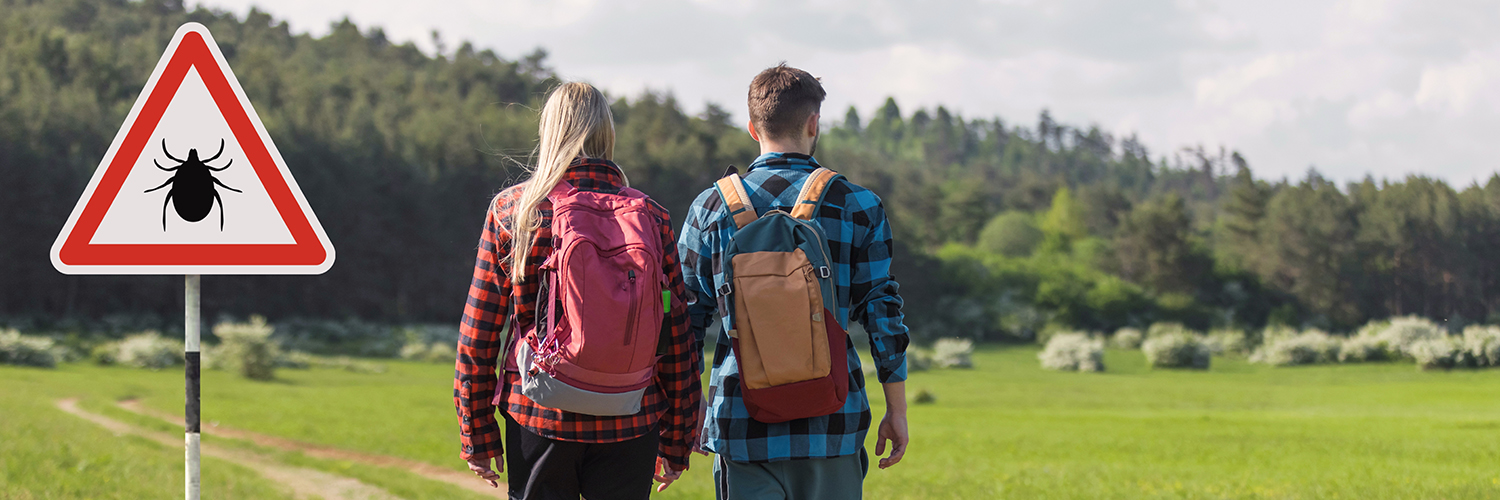 A young man and woman walking outdoors past a sign with a tick icon on it.