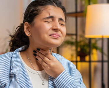 A woman holding her throat in pain while sitting at her desk at home.